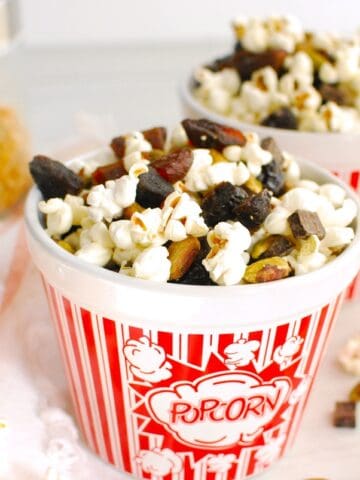 Two red and white popcorn bowls filled with popcorn trail mix.