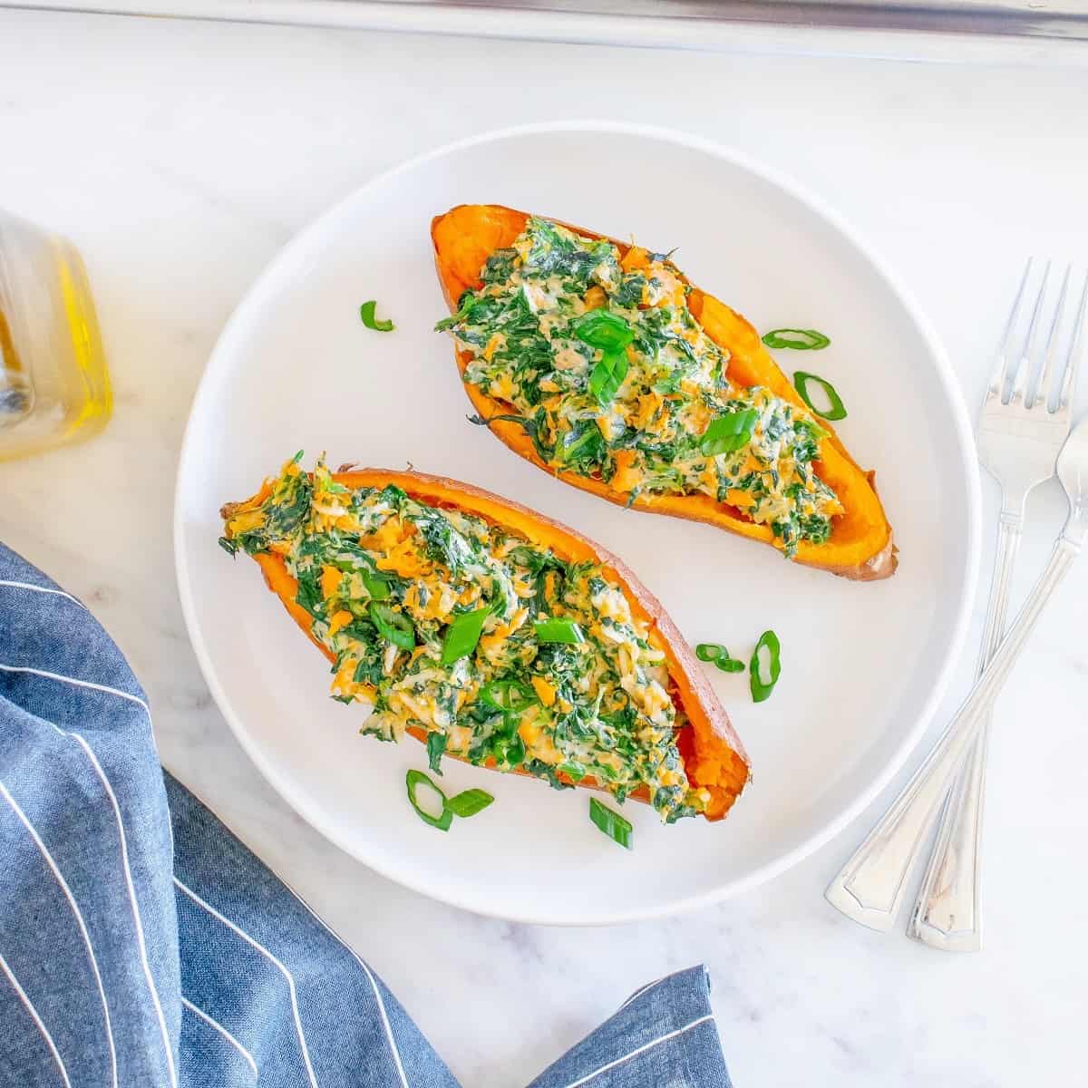 Two savory twice baked sweet potatoes on a white plate next to a blue napkin.