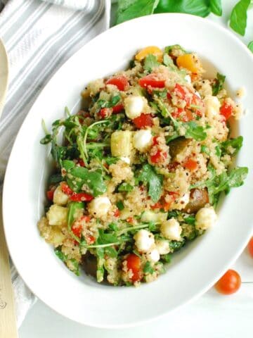 An overhead shot of a serving bowl of Italian quinoa salad next to a napkin and wooden serving spoon.