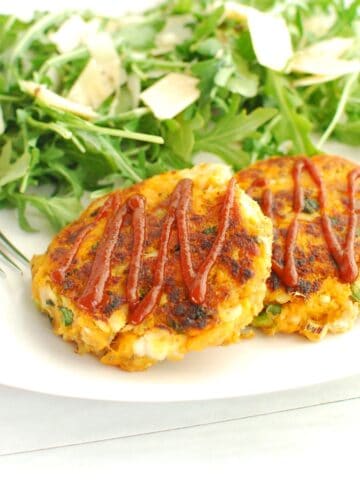 Two sweeptoato fish cakes on a plate next to a salad and a fork.