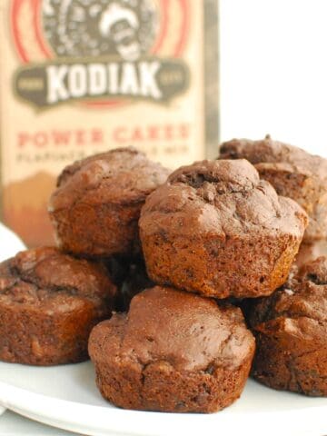 A plate with a bunch of dark chocolate protein muffins and a box of Kodiak cakes in the background.